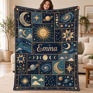 May include: A rectangular throw blanket featuring a dark blue celestial theme with gold accents. The design includes illustrations of the sun, moon, planets, stars, and galaxies arranged in panels. The name Emma is printed in gold script in the center.