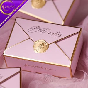 Può includere: Scatole regalo rosa a forma di busta, con bordi dorati e un sigillo di cera dorato. Le scatole presentano le scritte "Best Wishes" e "Special thanks to you."