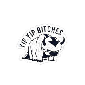 May include: A white sticker featuring a black and white illustration of a bison-like creature with the text "YIP YIP BITCHES" in a circular arrangement around the top. The creature has a dark arrow-shaped marking on its head.