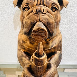 May include: A brown bulldog sculpture holding a candle holder. The bulldog has detailed fur texture and is holding the candle holder with both paws. The sculpture is set against a white wall.