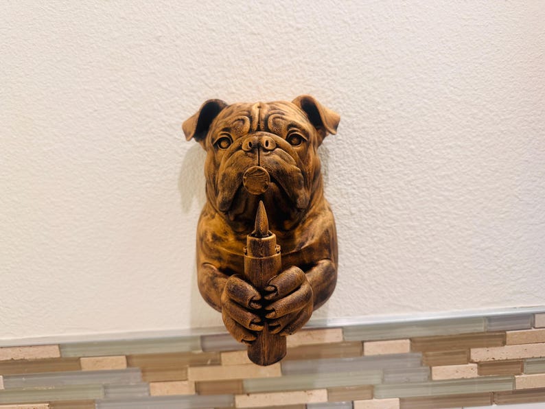 May include: A detailed, brown bulldog sculpture holding a wooden object. The bulldog's face is intricately carved, with visible wrinkles and a serious expression. The sculpture is mounted on a wall, showcasing its detailed craftsmanship.