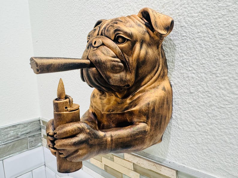 May include: A wall-mounted sculpture of a bulldog with a cigar in its mouth and a lighter in its paws. The sculpture is finished in shades of brown and gold, with detailed textures. The bulldog's expression is stoic.