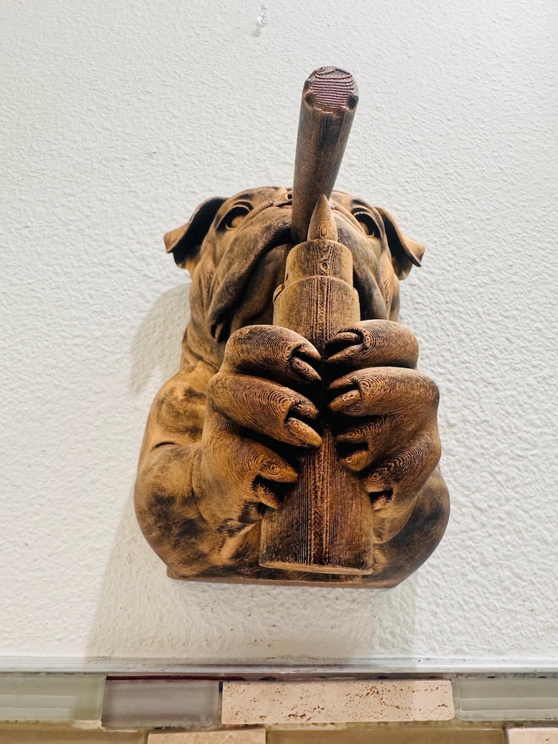 May include: A brown sculpture of a bulldog holding a long, cylindrical object to its mouth. The bulldog's paws are wrapped around the object. The sculpture is mounted on a white wall.