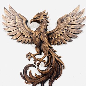 May include: A bronze-colored phoenix sculpture with outstretched wings and detailed feathering. The bird's talons are visible, and the tail feathers curl elegantly. This wall art piece is a decorative item.