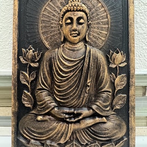 Peut inclure: Une œuvre d'art murale rectangulaire représentant une sculpture de Bouddha assis en méditation. La sculpture est dans des tons or et marron, sur un fond noir avec un cadre doré. Des fleurs de lotus encadrent le Bouddha.