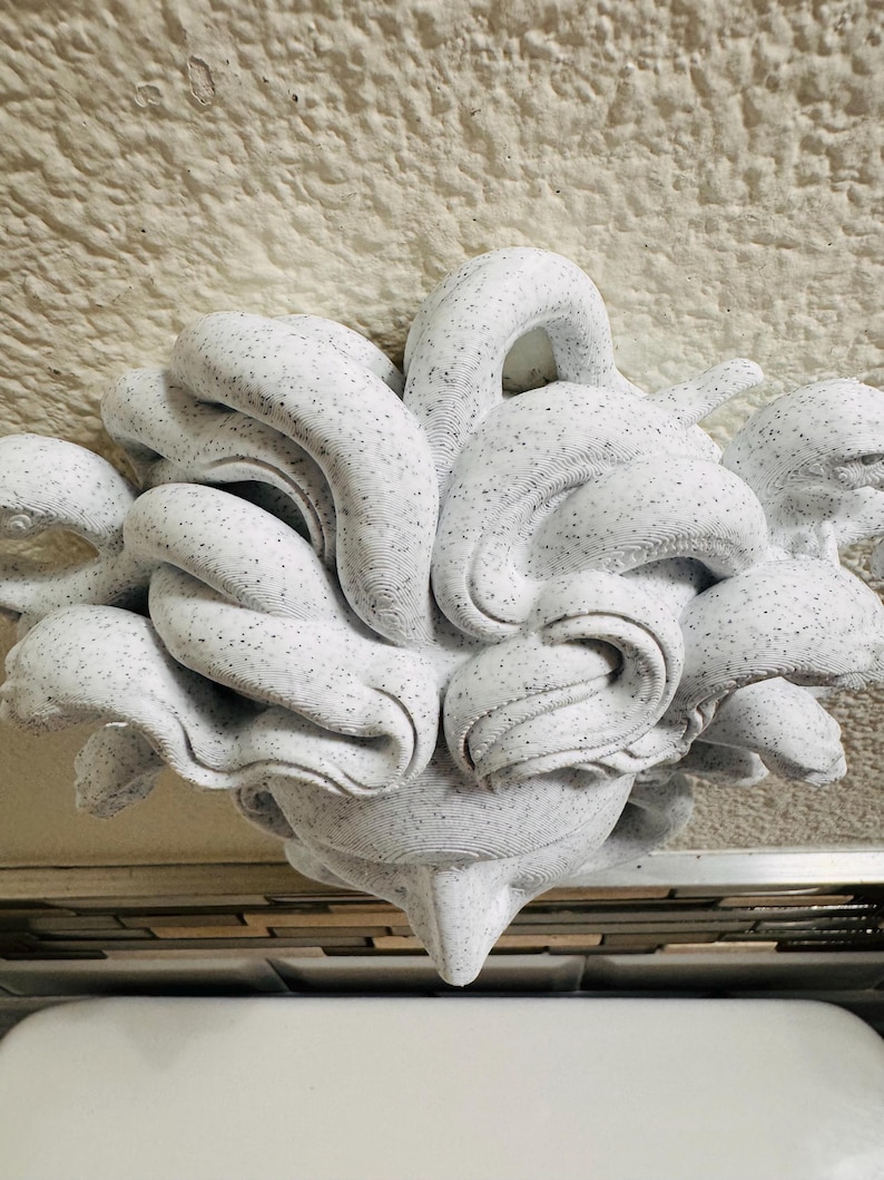 K&ouml;nnte beinhalten: Eine abstrakte wei&szlig;e Skulptur mit einem gesprenkelten Muster. Die Skulptur hat eine komplexe, organische Form mit abgerundeten Formen und einer spitzen Basis. Das St&uuml;ck scheint aus einem festen Material zu bestehen und ist vor einem neutralen Hintergrund platziert.