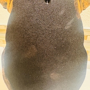 May include: A decorative wall hanging in the shape of a dog's head, featuring a textured, dark brown body and tan ears. The back has a keyhole for hanging.