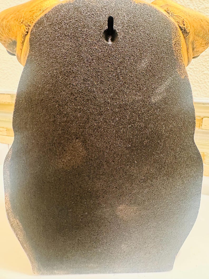 May include: A decorative wall hanging in the shape of a dog's head, featuring a textured, dark brown body and tan ears. The back has a keyhole for hanging.