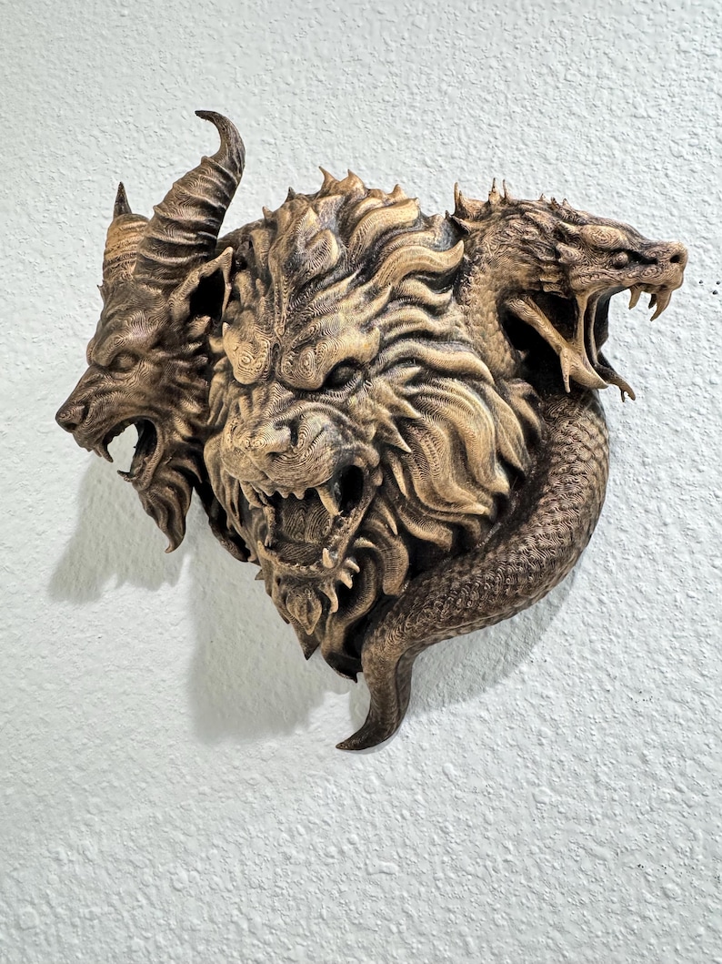 May include: A detailed, bronze-colored wall sculpture depicting a mythical creature with three heads: a goat, a lion, and a serpent. The sculpture has intricate details and is mounted on a textured white wall.