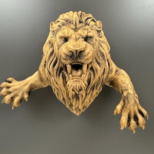 May include: A detailed, tan-colored lion sculpture with an open mouth, revealing teeth. The lion's mane is textured, and its paws are extended. The sculpture is likely made of resin or a similar material, and is designed to be mounted on a wall.