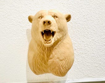 May include: A detailed, light brown bear head sculpture with an open mouth, revealing teeth and a detailed tongue. The bear's fur is textured, and the sculpture is mounted on a white wall, showcasing a rustic, wildlife-themed decor.