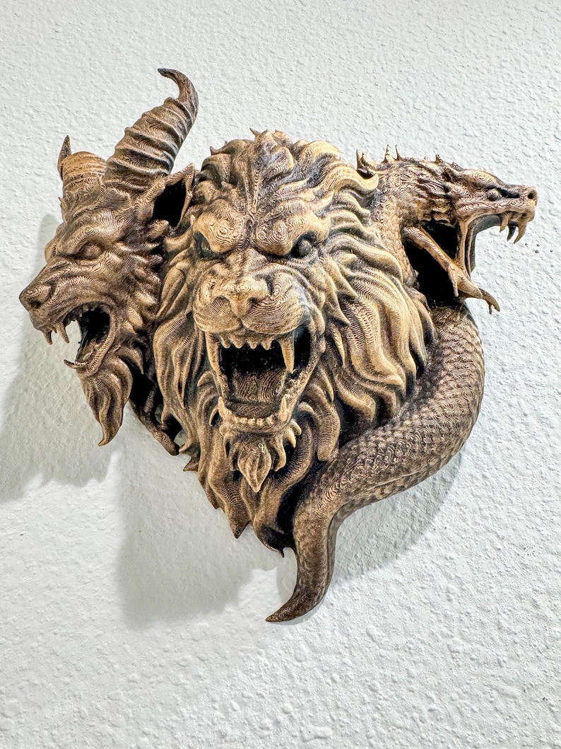 May include: A detailed, bronze-colored wall sculpture depicting a mythical creature with three heads: a lion, a wolf, and a dragon. The sculpture has intricate textures and is mounted on a white wall.