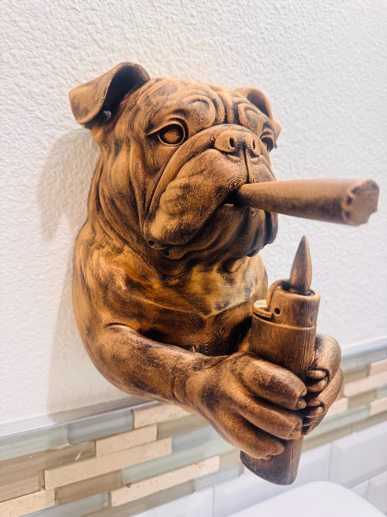 May include: A brown bulldog sculpture with a cigar in its mouth and a lighter in its hand. The sculpture is mounted on a white wall with a decorative tile border. The bulldog has detailed fur and facial features.