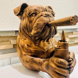 May include: A brown bulldog sculpture with a cigar in its mouth and a lighter in its hand. The sculpture has detailed textures and a realistic appearance, with a light source casting shadows.