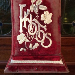 May include: A red velvet photo album with a white embossed design featuring the word "Photos" and floral accents.