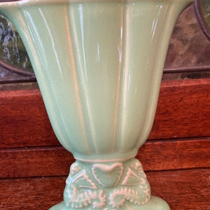 May include: A pale green ceramic vase with a fluted design and a decorative base with white floral accents.