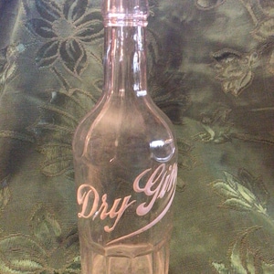 May include: A clear glass bottle with a white stopper. The bottle has a textured surface and the words "Dry Gin" are etched on the front.