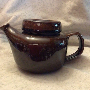 May include: A brown ceramic teapot with a rounded body and a spout. The teapot has a lid and a handle.