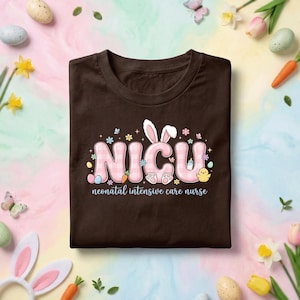 May include: A dark brown t-shirt with the word "NICU" in pink, checkered letters. The design includes bunny ears, flowers, eggs, a carrot, and a chick. The text "neonatal intensive care nurse" is below the main design.