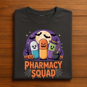 May include: Black t-shirt featuring a Halloween-themed graphic. The design includes three cartoon capsules with jack-o'-lantern faces, a witch's hat, bats, a full moon, and the words "PHARMACY SQUAD" in orange.