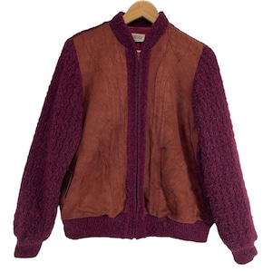 May include: A vintage bomber jacket with a brown suede-like front panel and deep burgundy knit sleeves and trim. The jacket has a full zipper closure and is hanging on a wooden hanger.