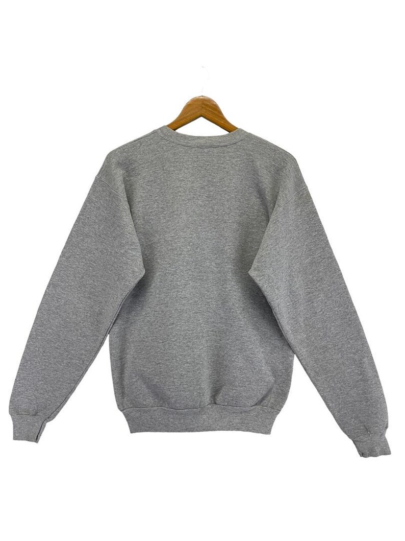 May include: A grey sweatshirt with a crew neck and long sleeves, suspended from a wooden hanger. The rear view of the garment reveals its plain, classic design. The material looks soft and comfortable. The colour is a medium grey.
