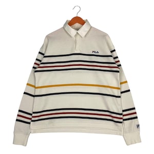 May include: A long-sleeve polo shirt in off-white featuring horizontal stripes in navy blue, dark red, and mustard yellow. The shirt has a collared neckline with a button placket and the FILA logo embroidered in navy blue on the upper left chest.