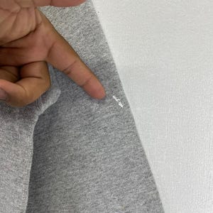 May include: Close-up of a grey long-sleeve shirt. The fabric is a heathered grey colour. The shirt is next to a white surface.