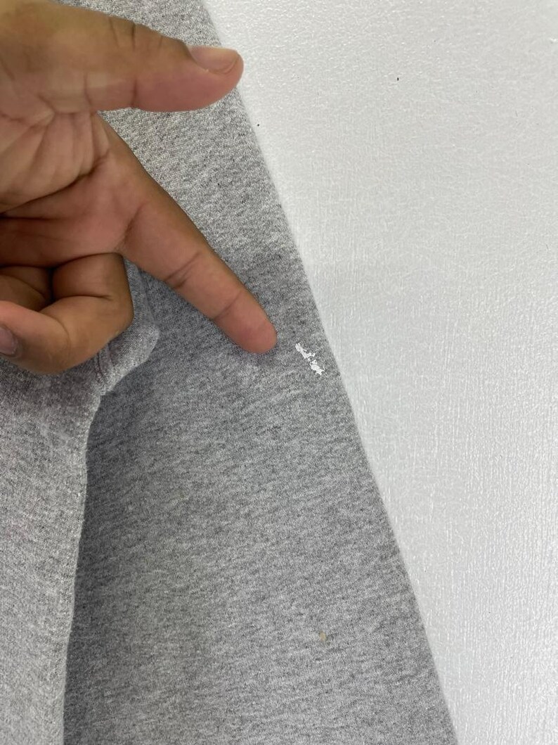 May include: Close-up of a grey long-sleeve shirt. The fabric is a heathered grey colour. The shirt is next to a white surface.