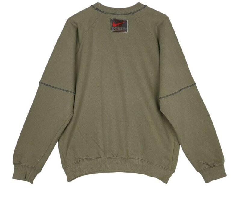 May include: Olive green sweatshirt with a crew neck and long sleeves. Features a stitched design on the sleeves and a red and black logo patch on the upper back. The sweatshirt has a relaxed fit.