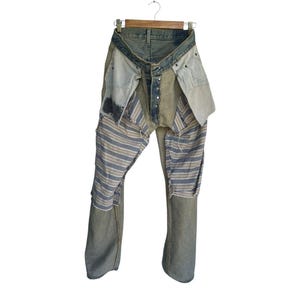May include: Distressed denim jeans with patchwork detailing. The jeans feature a light blue wash with various fabric patches, including striped and solid sections. The design includes visible seams and a button fly, creating a unique, deconstructed aesthetic.