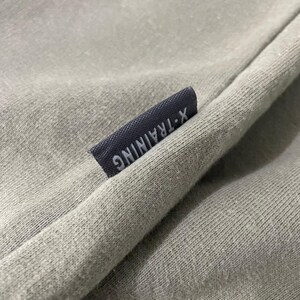 May include: Close-up of a light green fabric with a navy blue label. The label reads "X-TRAINING" in white capital letters. The fabric appears to be a soft, textured material, possibly cotton or a similar blend.
