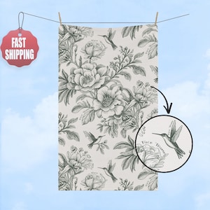May include: A white towel with a black and white floral and hummingbird pattern. The towel is hanging on a clothesline. The words "Fuck Trump" are written on the towel.