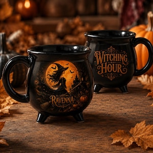 May include: Two black ceramic cauldron-shaped mugs with three small feet. One mug features a graphic of a witch on a broomstick against a full moon with the text "RAVENNA". The other mug displays the orange text "WITCHING HOUR" in a decorative font.