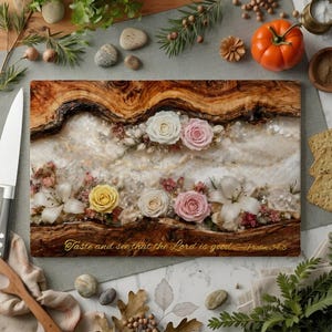 May include: A rectangular wooden cutting board with a floral design. The board features white, pink, and yellow roses, white lilies, and the text "Taste and see that the Lord is good - Psalm 34:8".