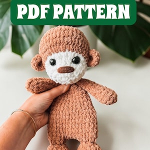 Op de afbeelding: Een handgemaakte, pluche aap in bruin- en wittinten. De aap heeft een getextureerde, fuzzy uitstraling, met een wit gezicht, een bruine neus en zwarte ogen. De tekst "PDF PATTERN" wordt weergegeven in een groene rechthoek boven de aap.
