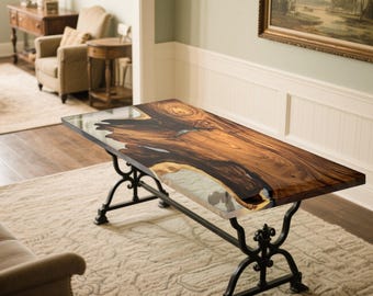 Può includere: Un tavolino rettangolare con piano in legno a bordo vivo e intarsio in resina trasparente. Il legno è di un ricco colore marrone con motivi di venature scure. Il tavolo ha una base in ferro battuto nero con decorazioni a volute.