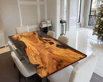 May include: A rectangular dining table with a live edge wood top and a dark resin fill. The table is surrounded by six white upholstered chairs. The wood grain is a mix of light and dark brown tones.