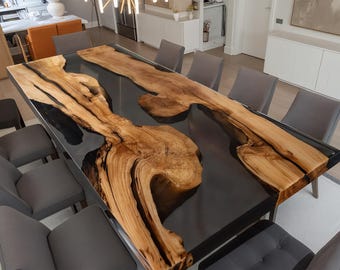 May include: A large, rectangular dining table with a unique design. The tabletop features a dark gray resin base with natural wood grain patterns. The table is surrounded by gray upholstered chairs, creating a modern and elegant dining space.