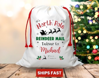 May include: White Christmas gift bag with red drawstring closure. The bag features the text "North Pole Reindeer Mail" and "Deliver to: Michael" in red and green. Includes a "Nice List" and "Naughty List" check boxes. The bag is on a wooden surface.