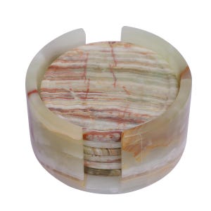 May include: A set of circular stone coasters stacked inside a matching cylindrical stone holder. The coasters and holder feature a polished finish with natural banded patterns in shades of cream, white, pale green, and reddish-brown mineral veins.