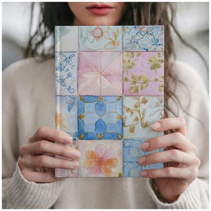 May include: A square notebook with a watercolour tile design. The cover features a grid of colourful squares with floral and geometric patterns in shades of blue, pink, and orange. The notebook is held by a person wearing a cream-coloured sweater.