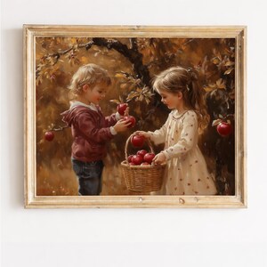 以下が含まれることがあります： 額縁に入った絵画で、2人の子供が木から赤いリンゴを収穫している様子が描かれています。一人はマルーン色のパーカーとジーンズを着ており、もう一人はクリーム色のドレスを着ています。編まれたバスケットにはリンゴがいっぱいです。