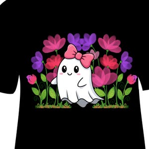 Puede incluir: Camiseta negra con un fantasma de dibujos animados con un lazo rosa, sobre un fondo de flores rosas, rojas y moradas. El fantasma tiene una cara sonriente y está rodeado de elementos florales estilizados.