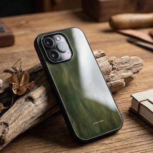 May include: A green and black phone case with a glossy finish. The case has a black border and a clear back, showcasing the phone's camera lenses. The text "MIROT STUDIO" is visible on the bottom of the case. The case is on a wooden surface.