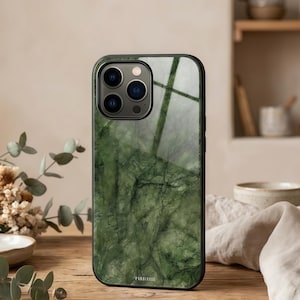 May include: A smartphone case with a green marble design. The case has a black border and a glossy finish, with a pattern of dark green veins and swirls. The phone's camera lenses are visible at the top. The brand name is printed at the bottom.