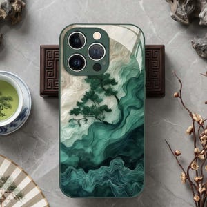 Puede incluir: Funda de teléfono verde y blanca con un diseño de paisaje abstracto con un árbol. La funda tiene un acabado brillante y un recorte para la cámara. El diseño incorpora tonos verdes y blancos, creando una estética serena.