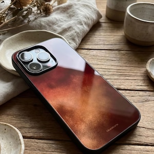 May include: A smartphone case with a gradient design in shades of red, orange, and brown. The case has a black border and the word "bluestone" is printed on the bottom. The phone's camera lenses are visible.