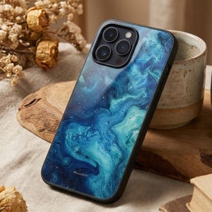 May include: A black phone case with a swirling blue and teal abstract design. The case has a glossy finish and a black border. The text "MoonHill" is printed at the bottom. The case is on a wooden surface.