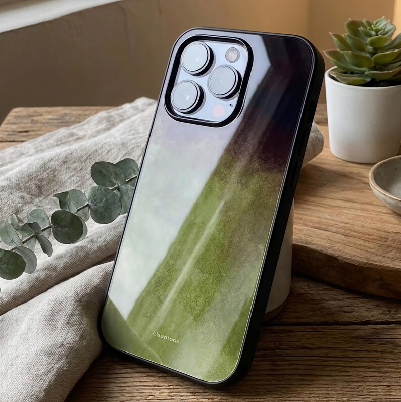 May include: A smartphone case with a green and white watercolor design. The case has a black border and a glossy finish. The brand name "bluaotone" is printed at the bottom of the case.